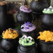 7 mini cauldron cakes which are green, orange and purple in color.