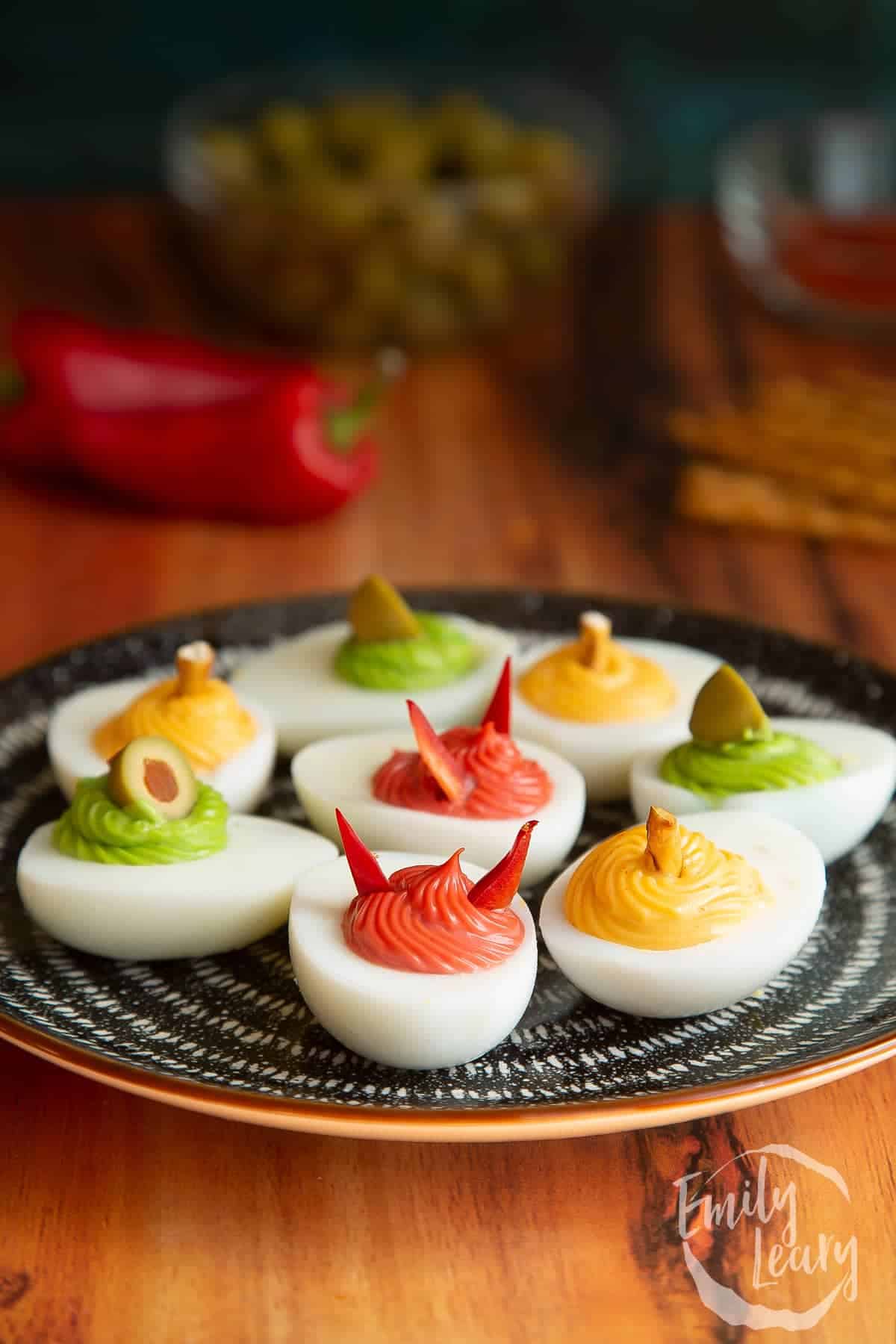 Green, red and yellow Deviled Eggs on a dark plate.