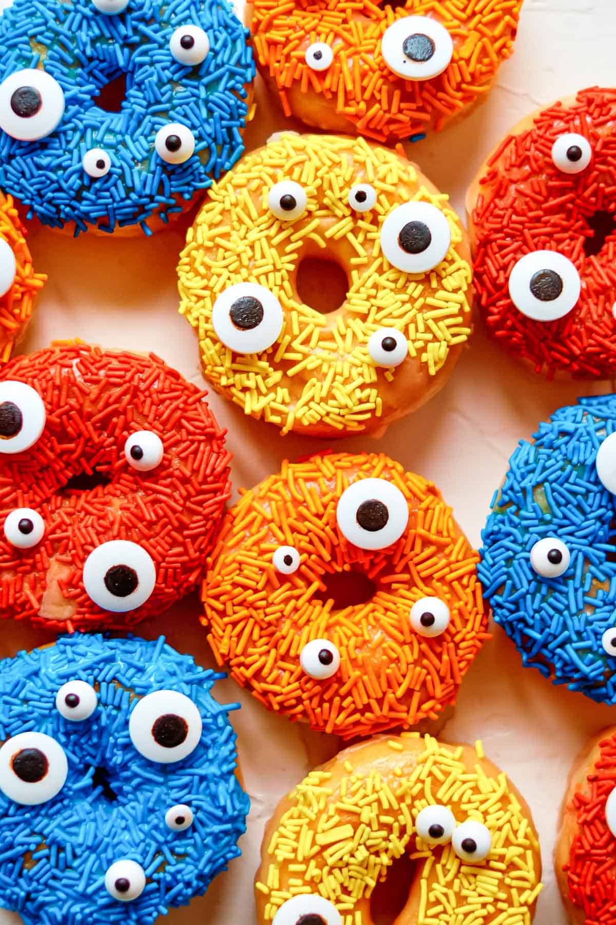 Blue, yellow, orange and red sprinkled donuts next to each other.