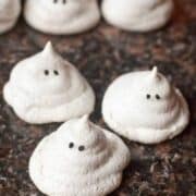 White meringues decorated as ghost on a brown marble top.