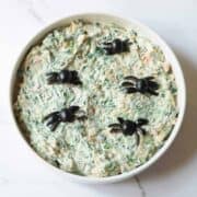 Spiders made of olives on a bowl of creamy spinach dip.