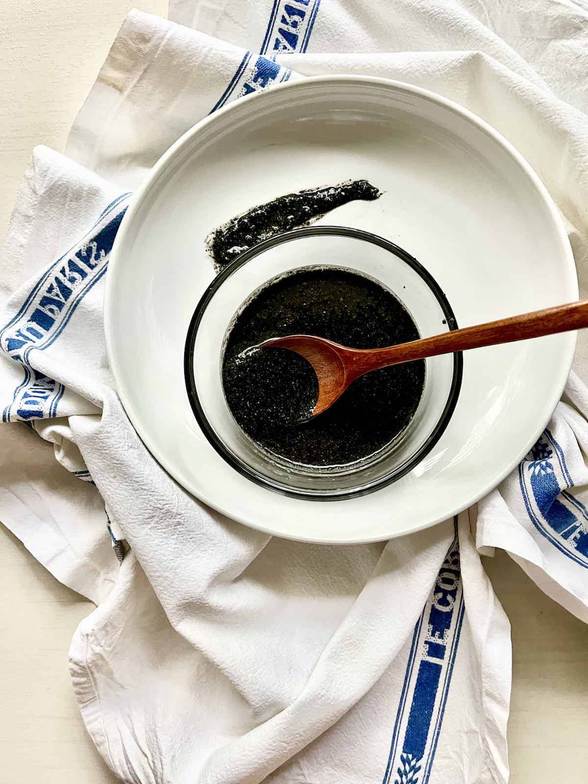 A glass jar full of ground black sesame paste with a wooden spoon in it.