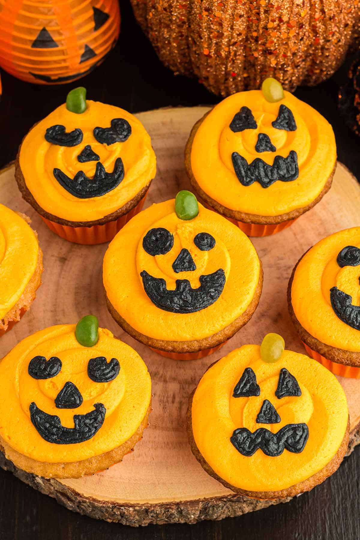 5 orange cupcakes decorated as Jack O Lanterns on a wooden log board.