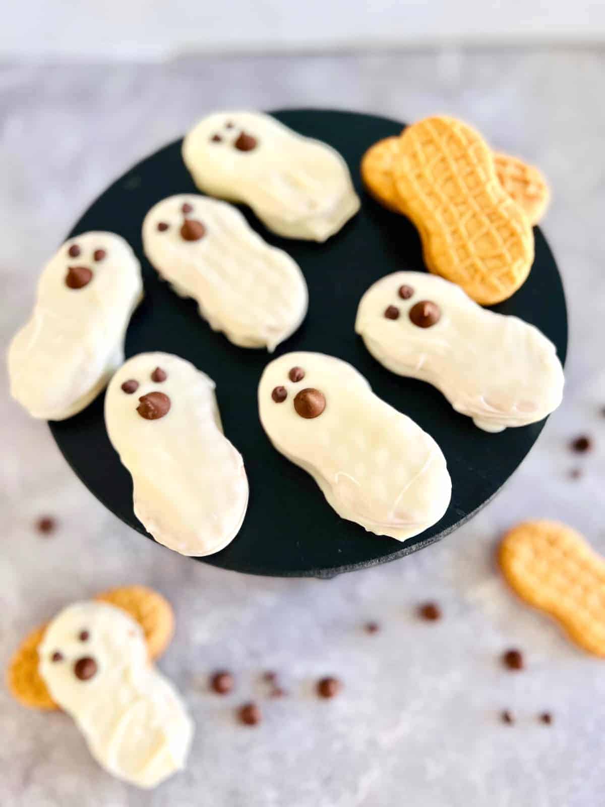 Ghost shaped white cookies on a black plate.