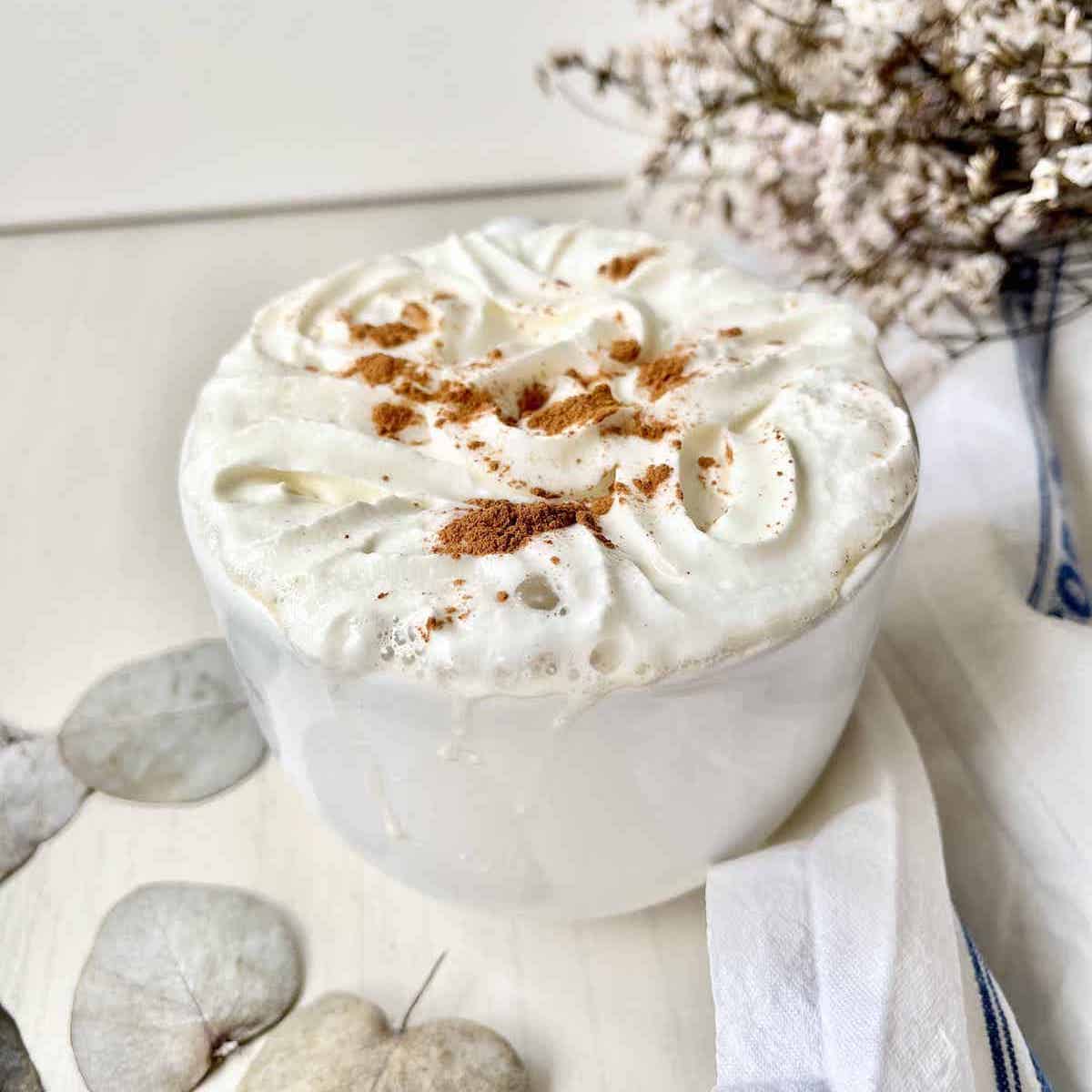 A cosy cup of peanut butter whipped cream topped with cinnamon sprinkle and cream.