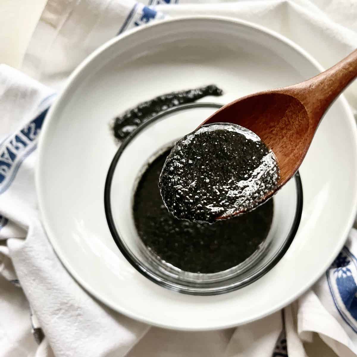 A wooden scoop of Black Sesame Paste with a white plate underneath.