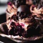Close-up of dark and eerie blackberry cupcakes decorated with chocolate skulls.