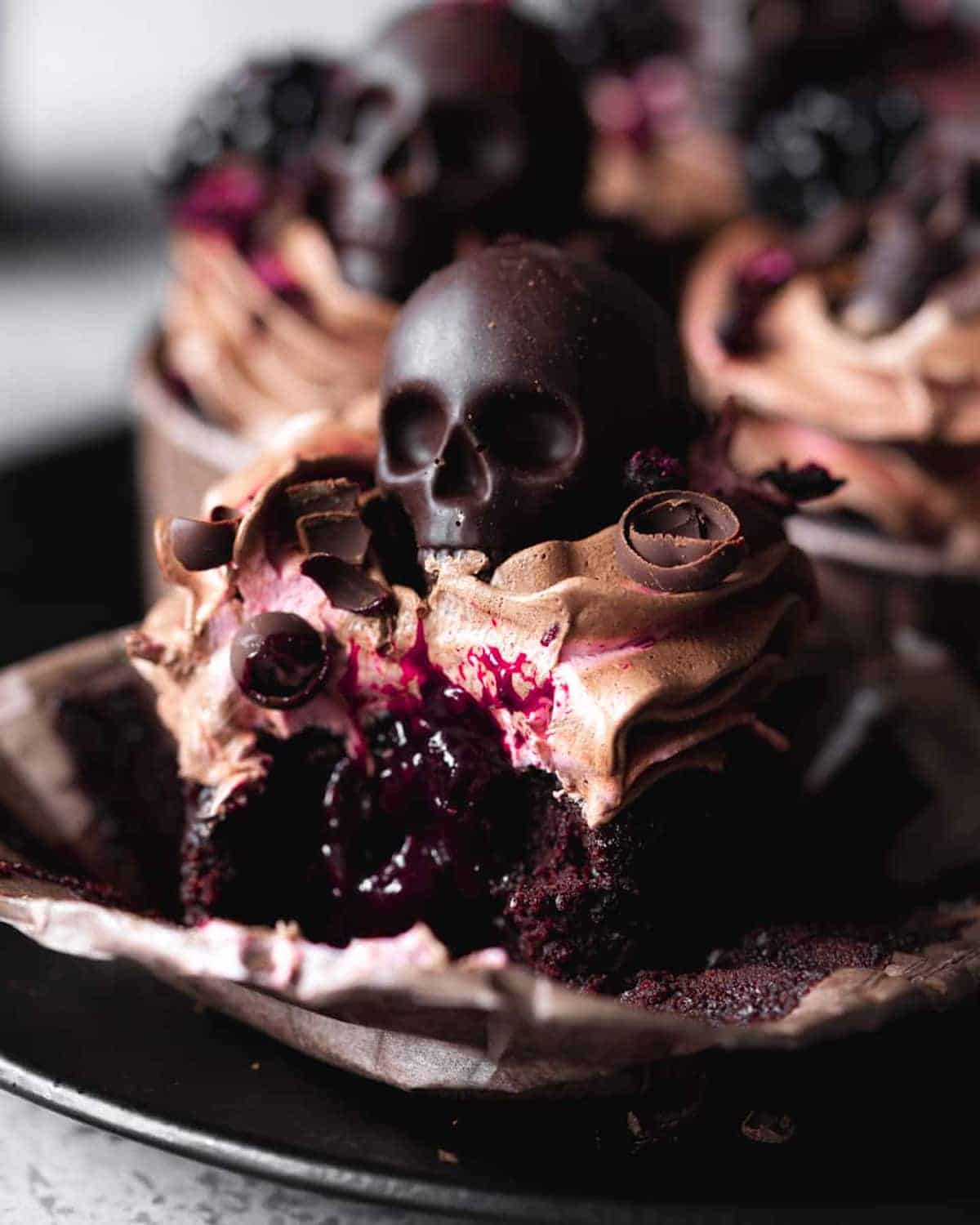 Close-up of dark and eerie blackberry cupcakes decorated with chocolate skulls.