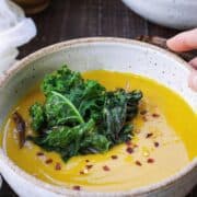 A bowl of golden kabocha soup with green kale on top.