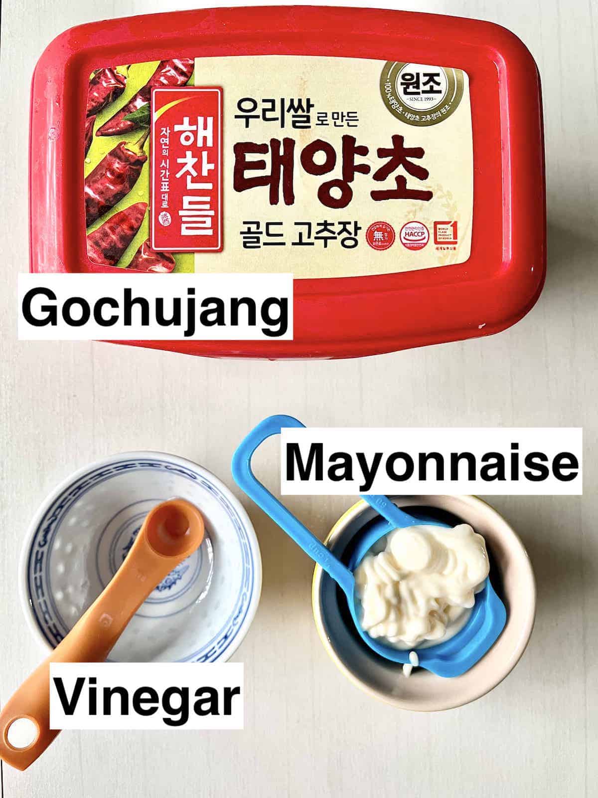 A box of Gochujang above a teaspoon of vinegar and a cup of mayo.