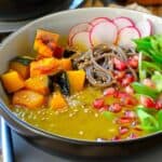 A bowl of soba noodles with Kabocha squash cubes and pomegranate seeds in a thick sauce.