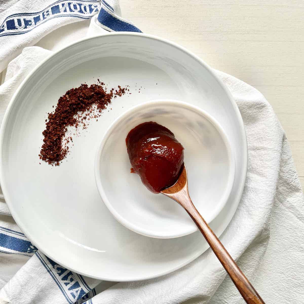 A tablespoon of Gochujang next to some red chili flakes.