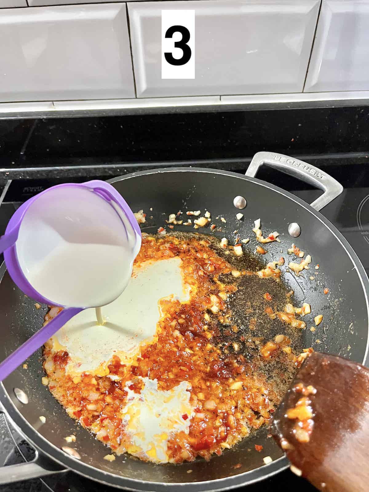 Adding a cup of heavy whipping cream to a pan of gochujang sauce.