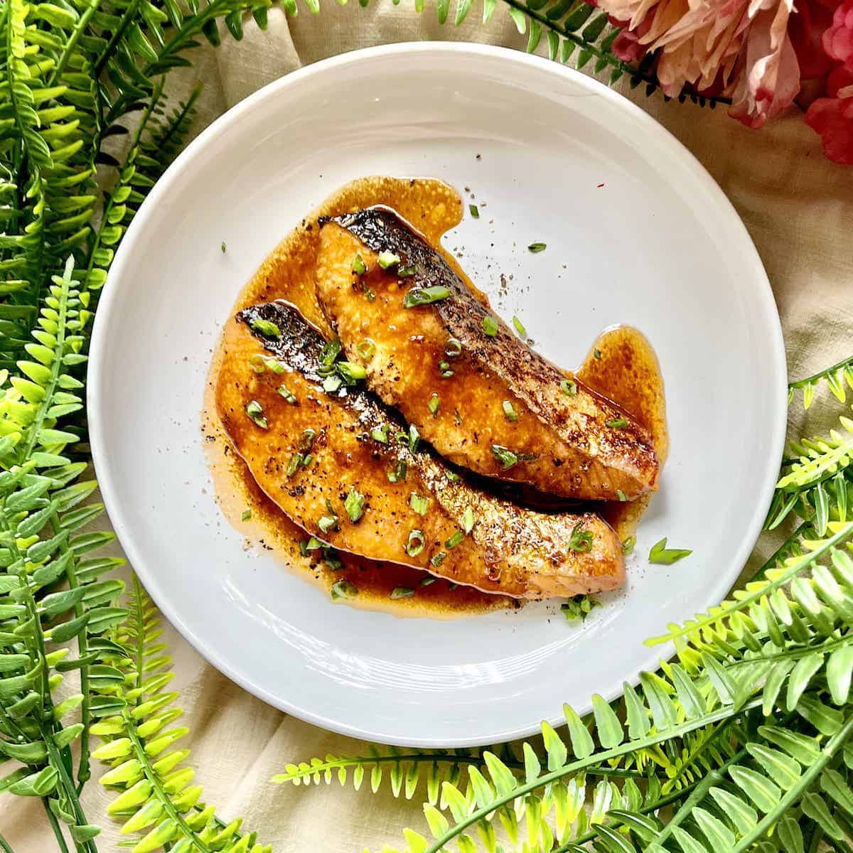 2 salmon fillets drizzled with teriyaki sauce on a white plate.