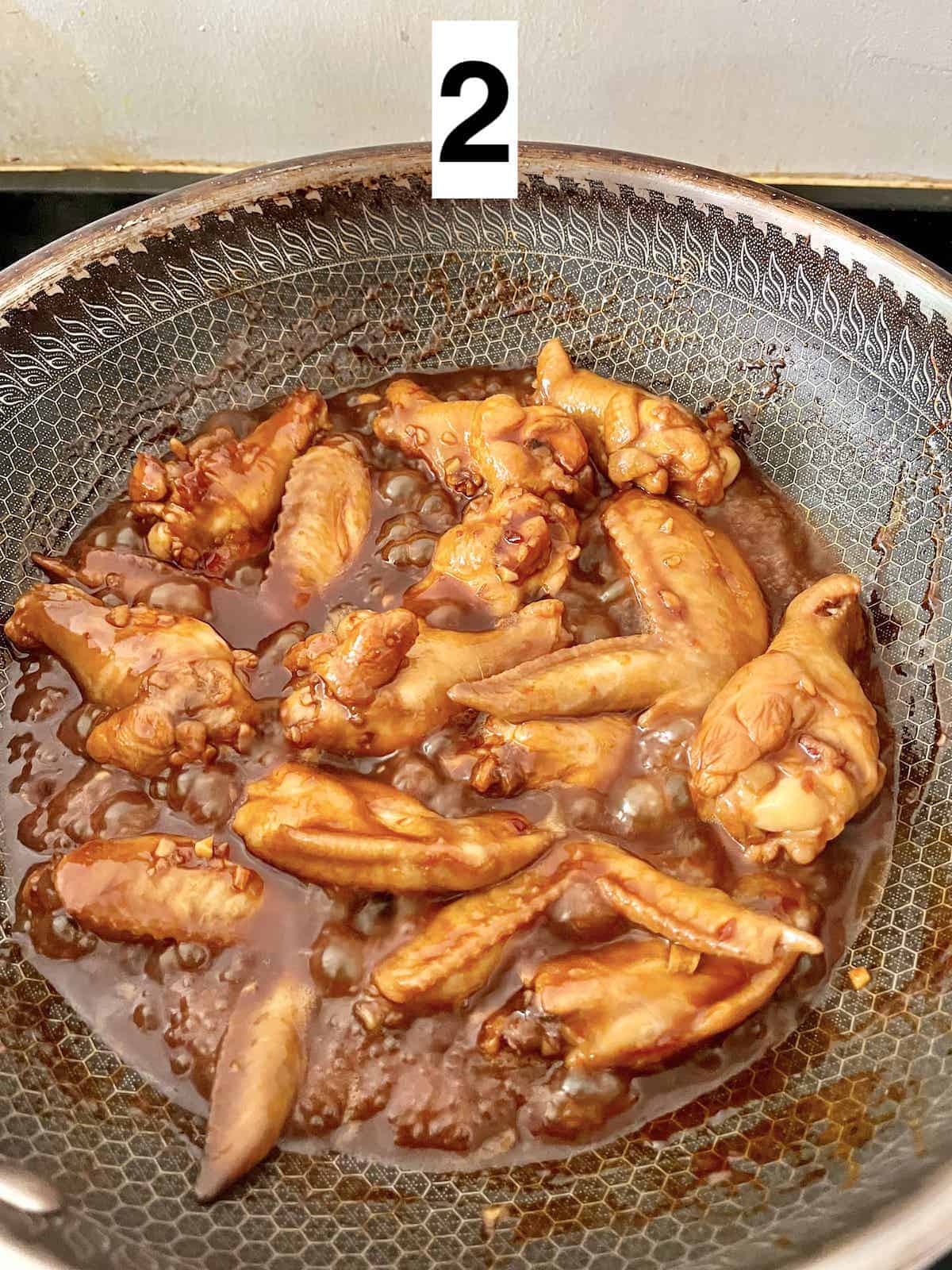 A wok full of braising chicken wings, separated into drums and flaps.