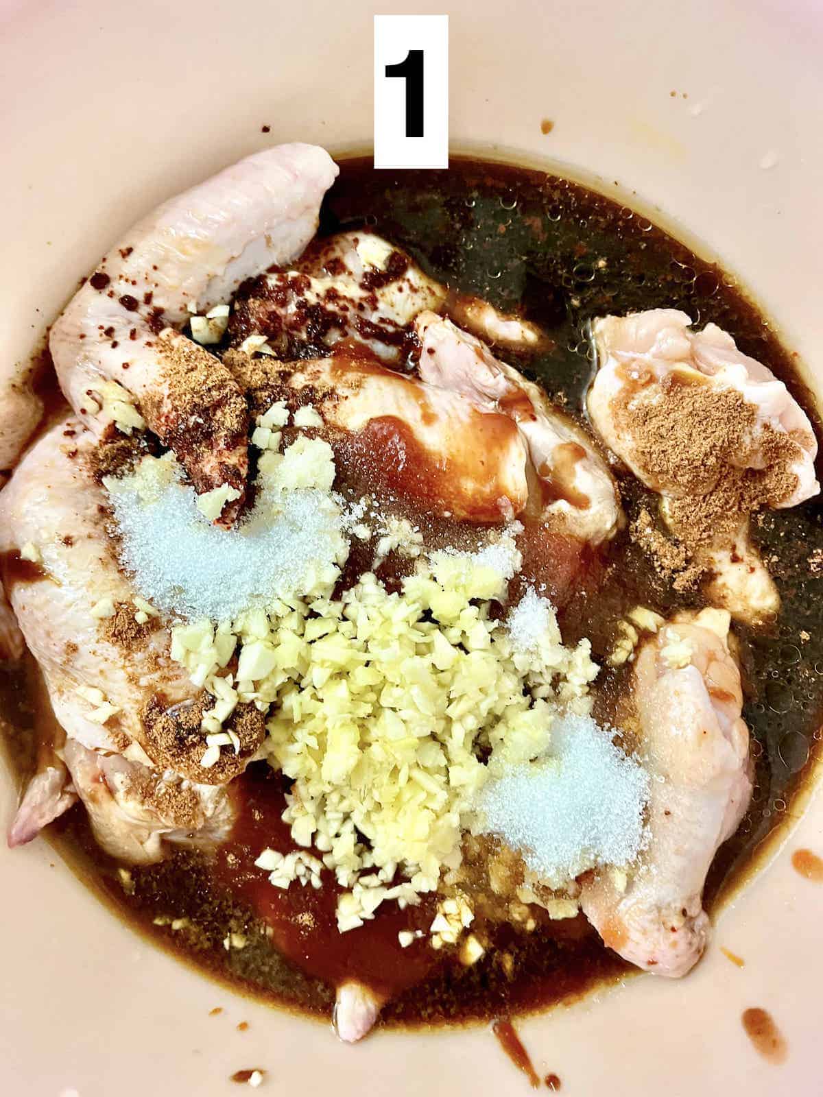 Overhead shot of a big bowl of chicken wings, garlic, sugar, and sauces.