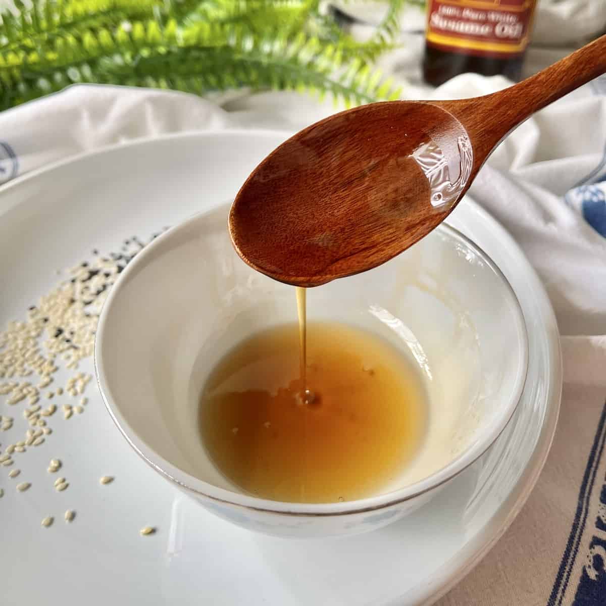A wooden spoon scooping sesame oil from a white bowl.