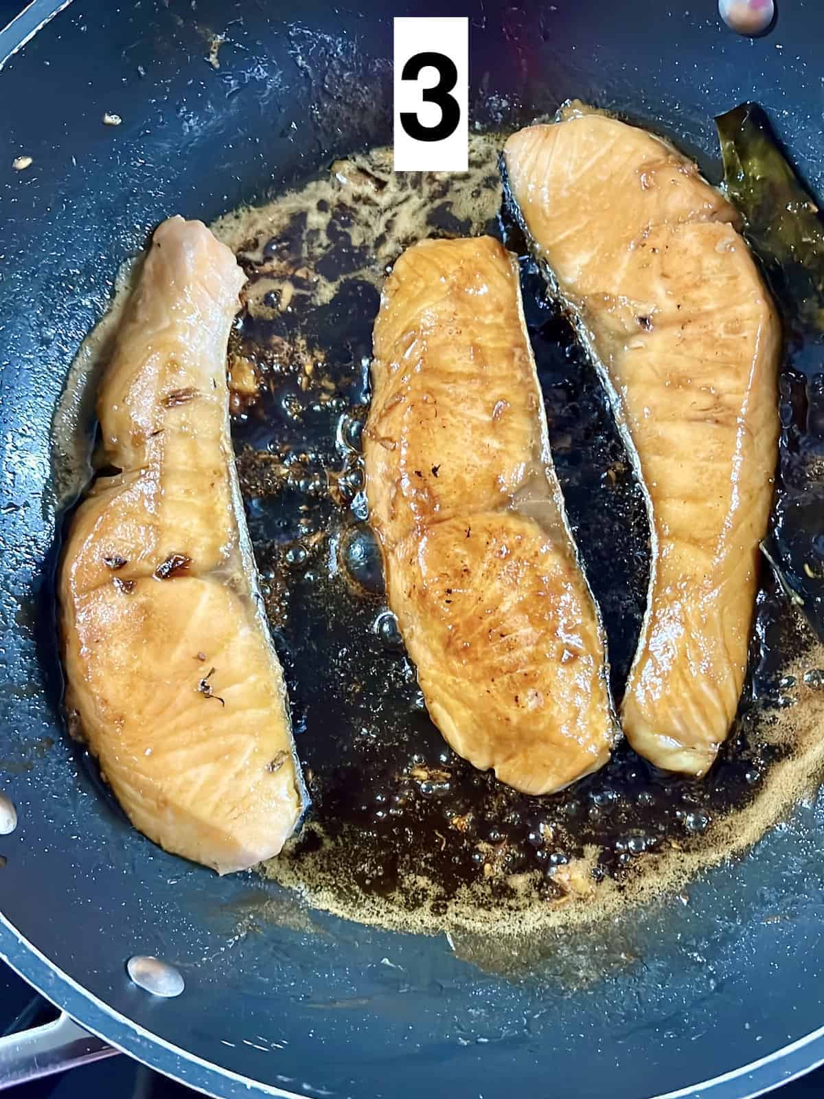 3 salmon filets in a pan with teriyaki sauce.