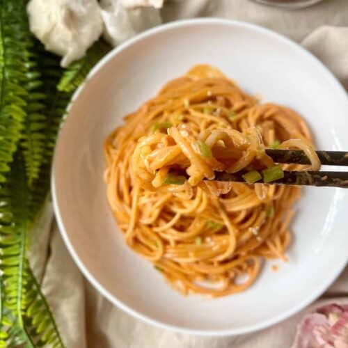 Close-up of a pair of chopsticks grabbing some spicy, red gochujang pasta noodles.