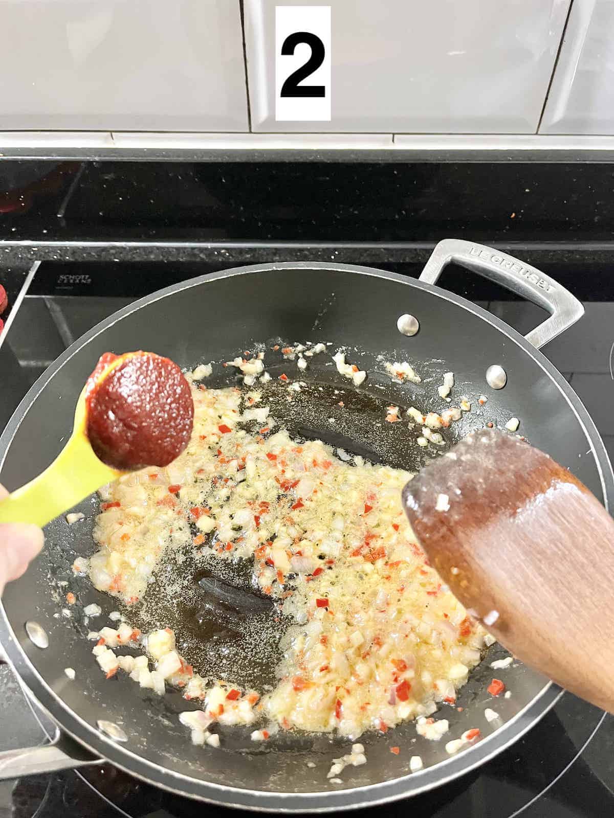 Adding a tablespoon of korean gochujang paste to a pan.