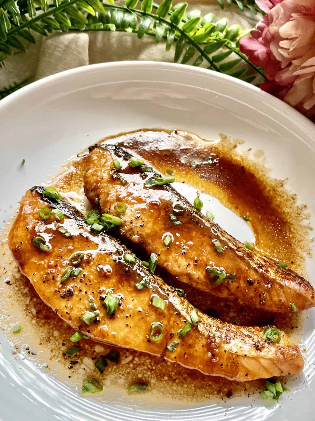 Close-up of 2 teriyaki salmon fillets with green onions.