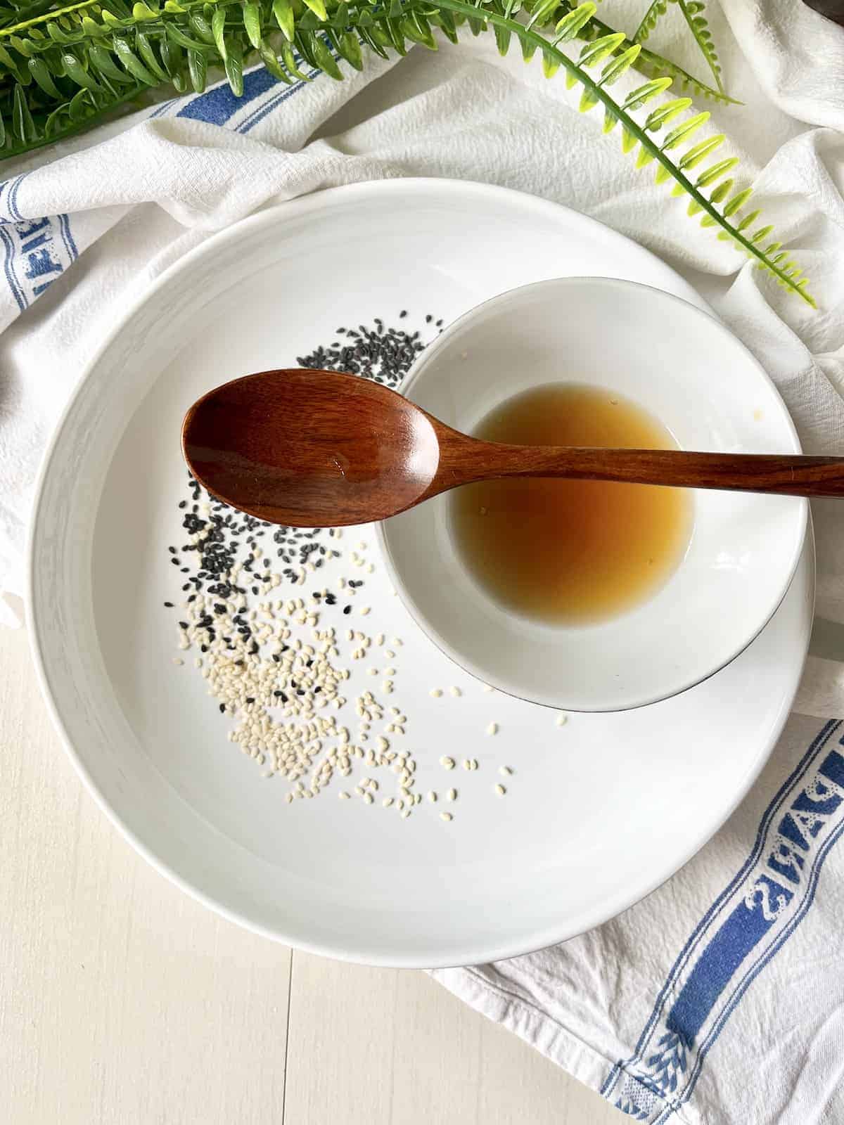 A bowl of homemade sesame oil next to white and black sesame seeds.