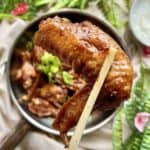 Close-up of a braised chinese chicken wing held up by a pair of chopsticks.