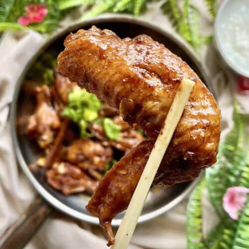 Close-up of a braised chinese chicken wing held up by a pair of chopsticks.