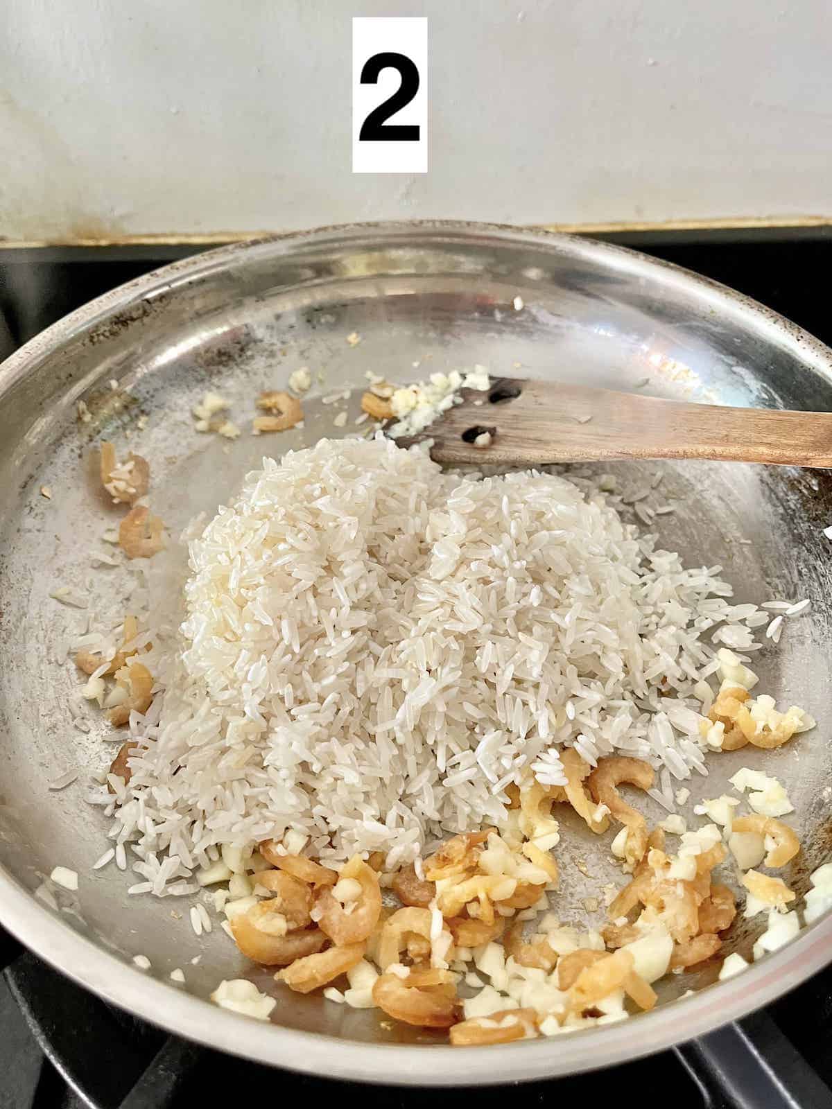 White rice grains being fried with garlic and Chinese dried prawns.