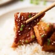 Close-up of a chopsticks picking up a tofu with spring onions on it.