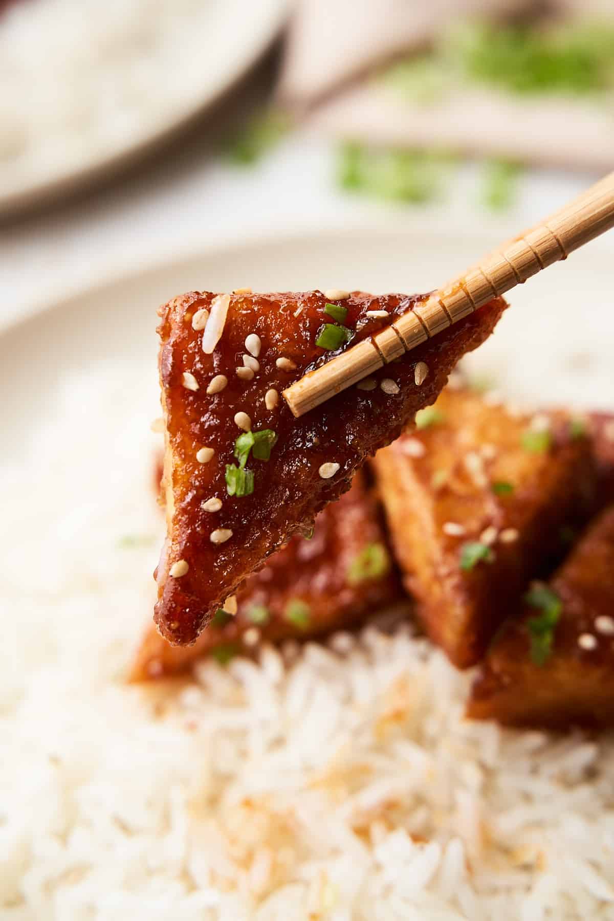 Close-up of a chopsticks picking up a tofu with spring onions on it.