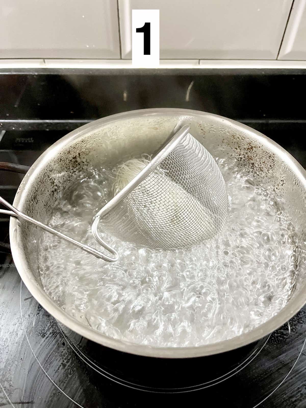 A bunch of bean thread vermicelli in a small sieve in a pot of boiling water.