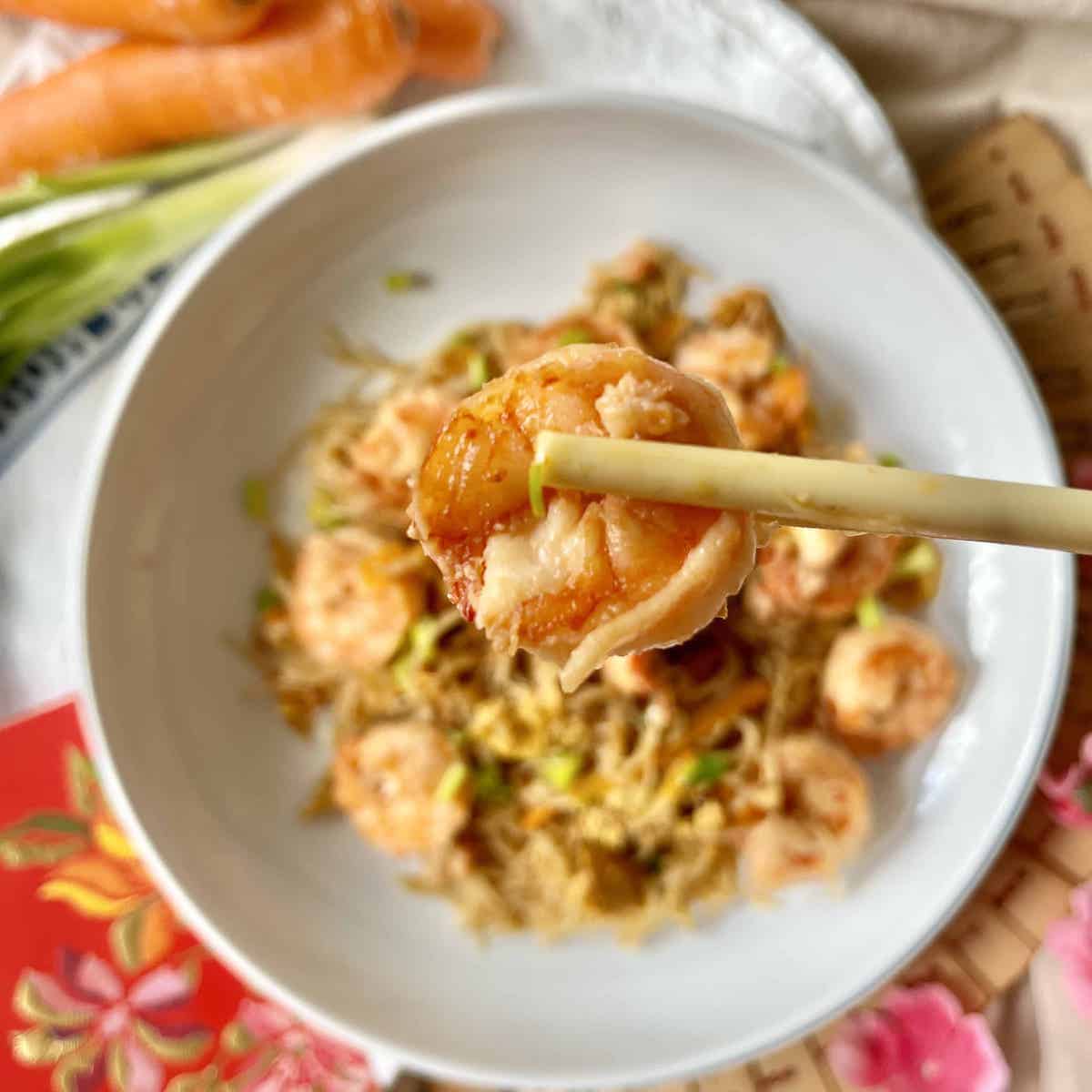 Close-up of chopsticks picking up a shrimp from a plate of shrimp Mei Fun.