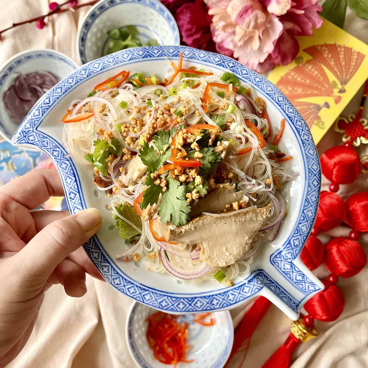 Vermicelli glass noodles mixed with sliced abalone, coriander, peanuts and dried shrimp on a leaf-shaped plate.