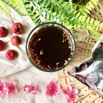 Overheat shot of a cup of Chinese Sour Plum Drink next to hawthorns and flowers.