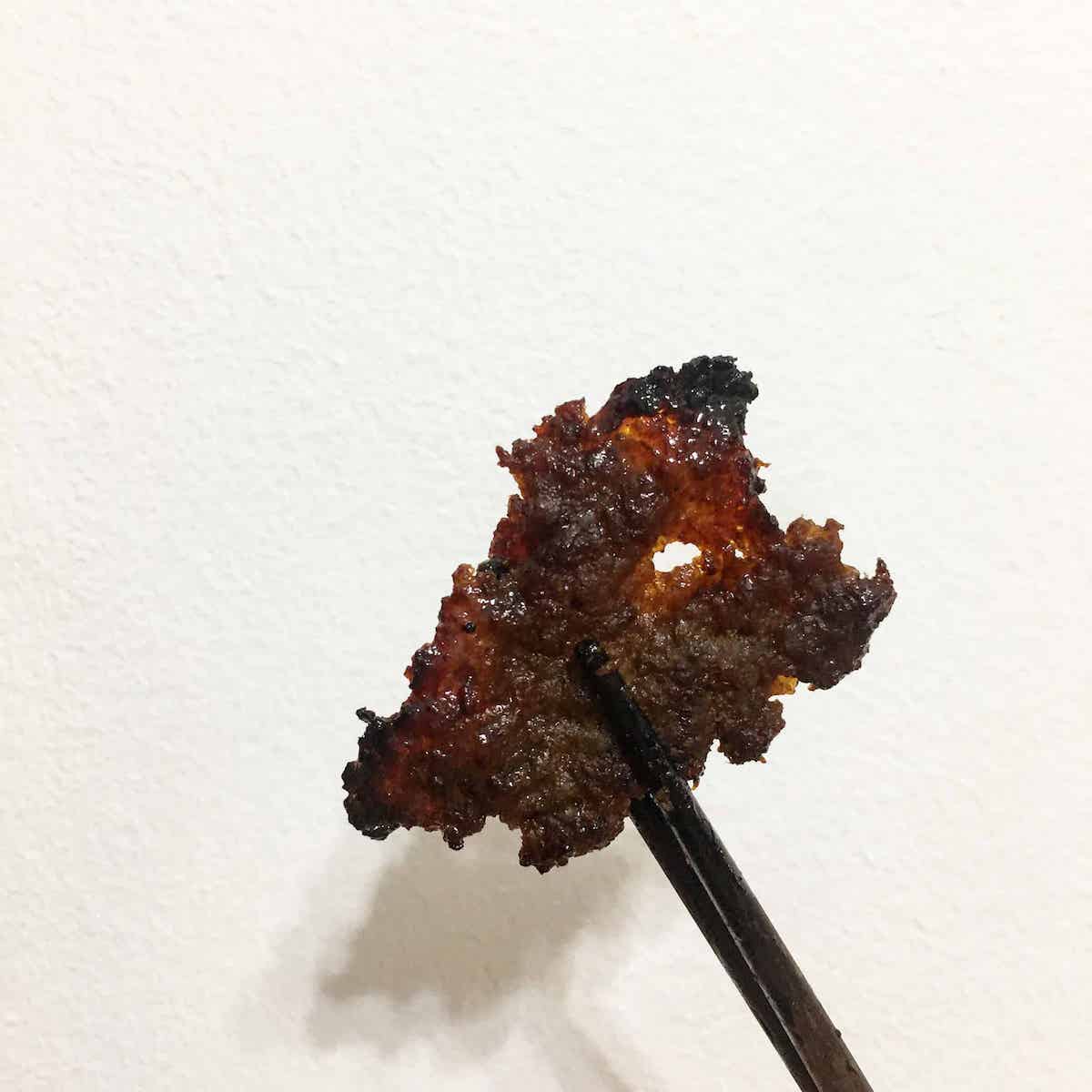 A pair of chopsticks holding a piece of homemade Bak Kwa.