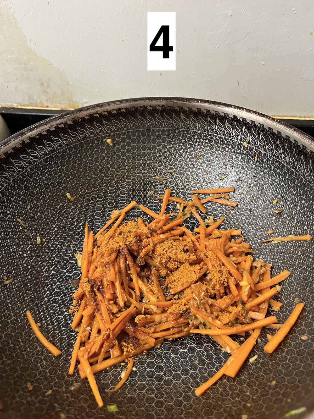 Thinly sliced carrots in a wok with curry powder.