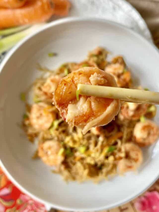 Close-up of chopsticks picking up a shrimp from a plate of shrimp Mei Fun.