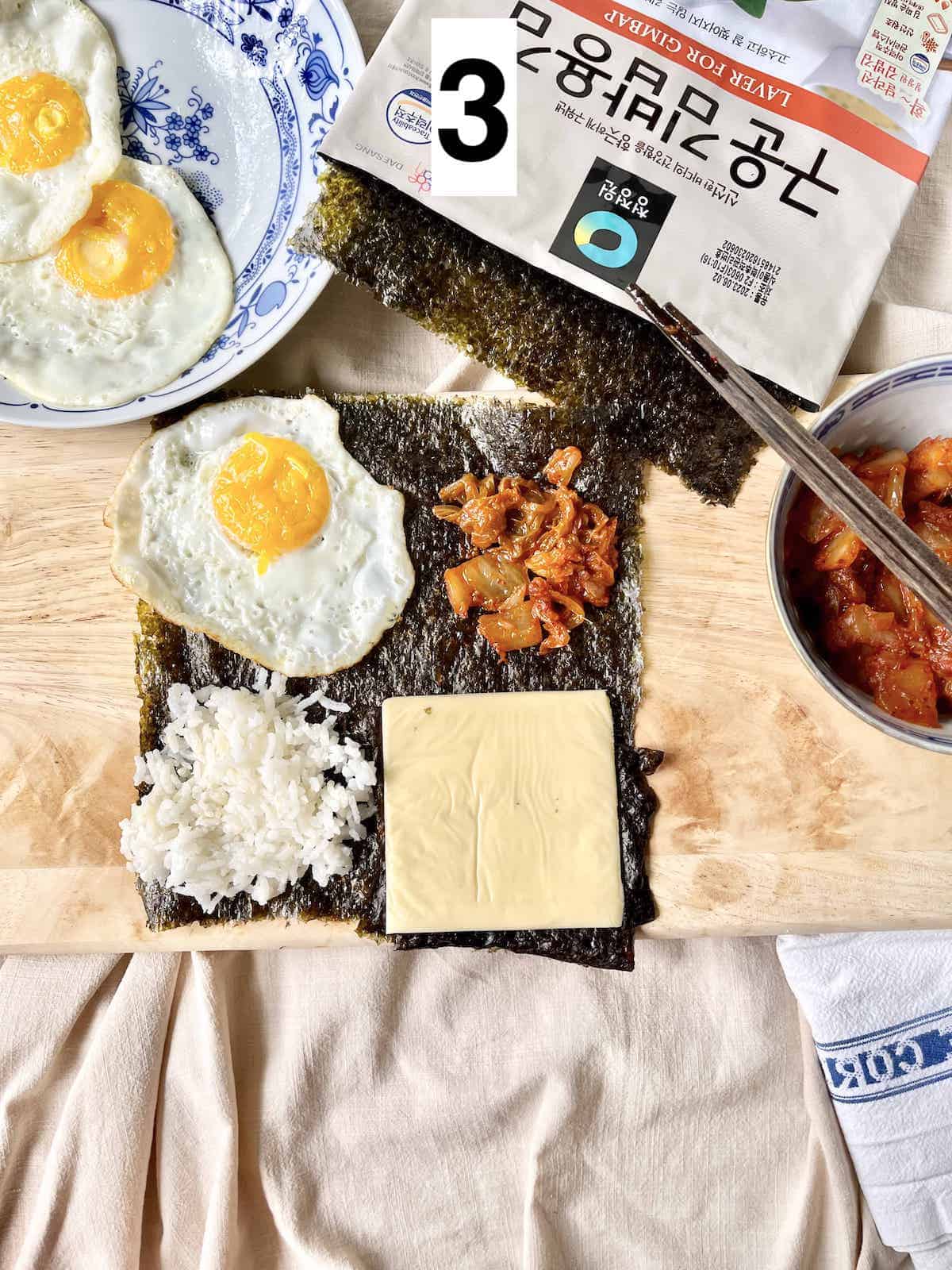 A piece of seaweed with an egg, rice, kimchi and cheese on it.