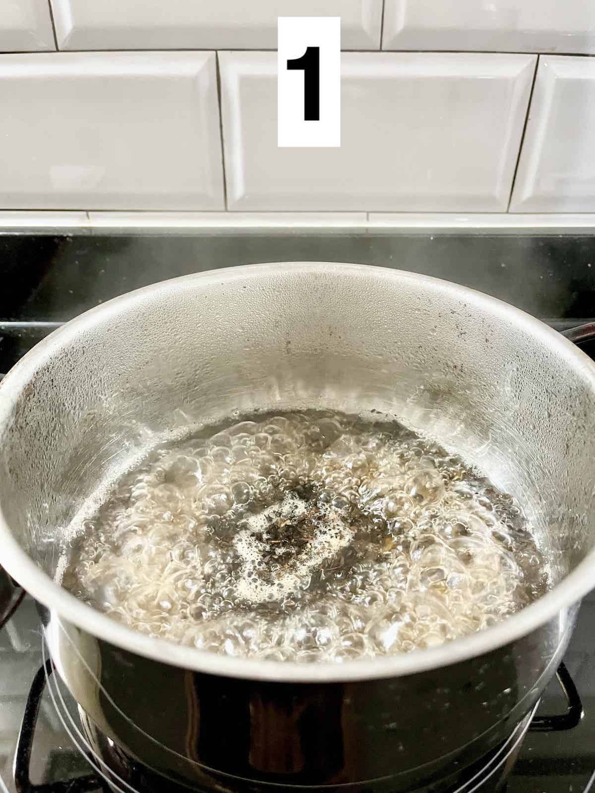 A pot of boiling water with black tea leaves inside on the stove.