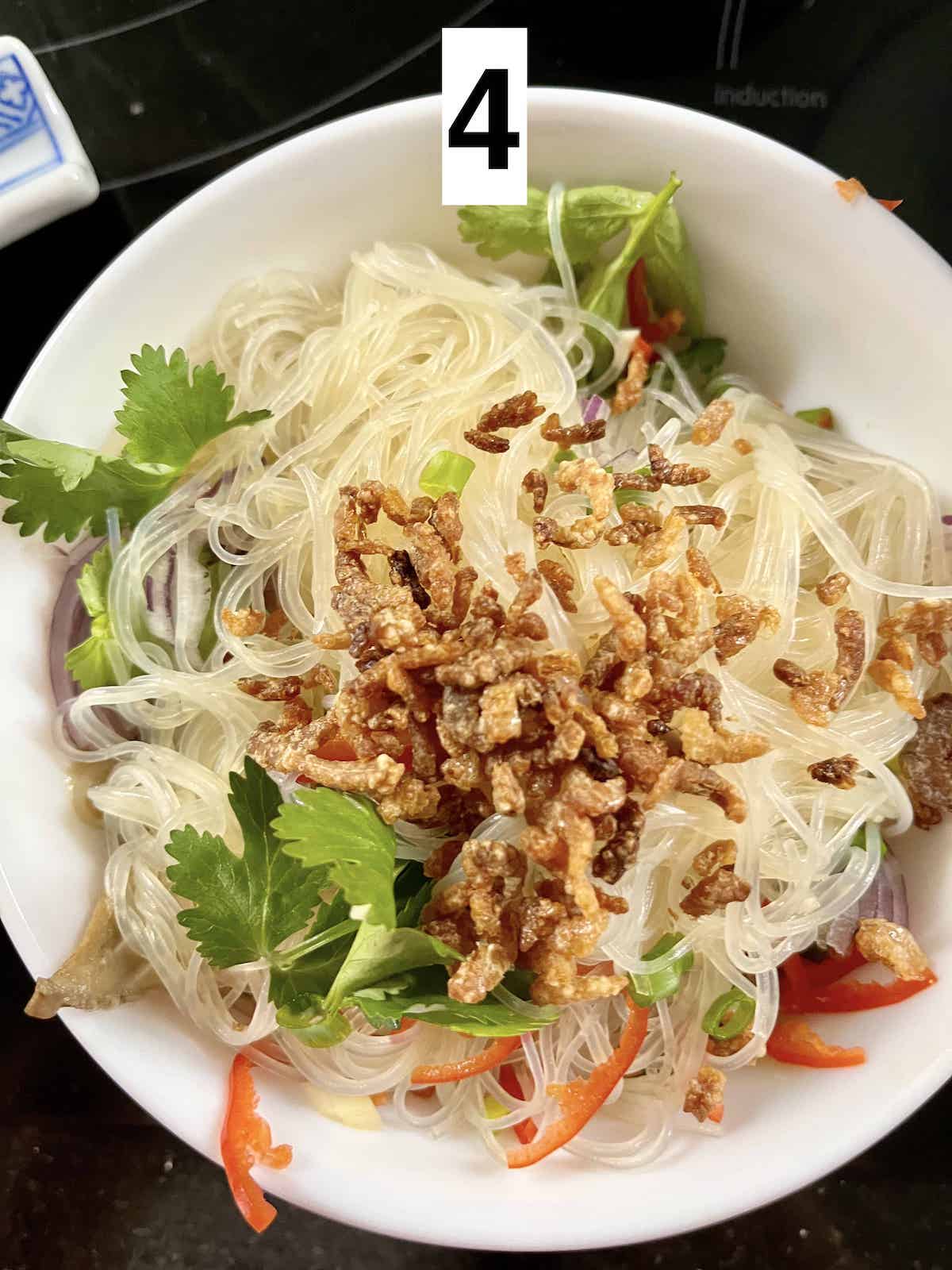 A bowl of glass noodles mixed with coriander, chili, spring onions and dried shrimp.