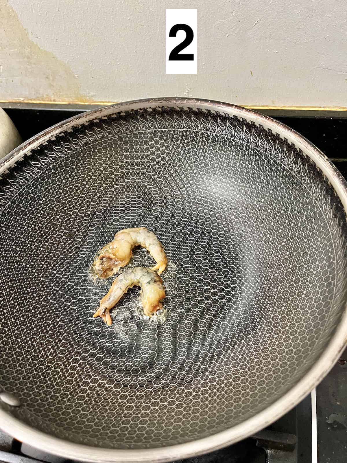 2 shrimps being stir-fried in a wok.