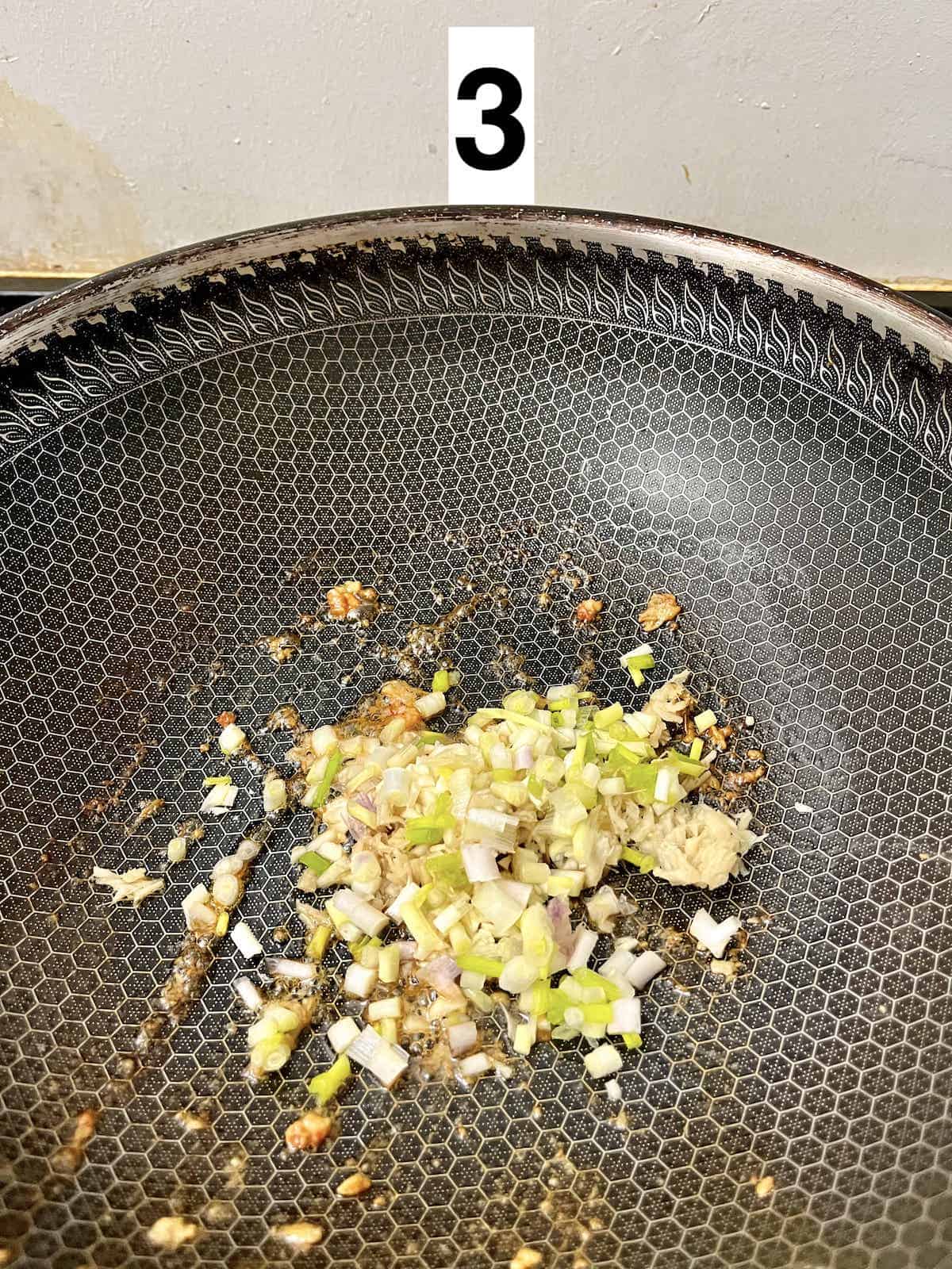 Spring onions, ginger and shallots being stir-fried in a wok.