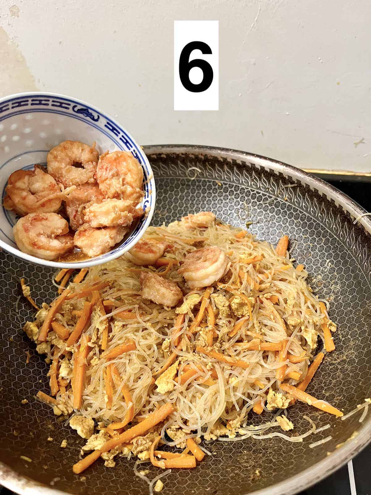 Adding cooked shrimp to a wok of Mei fun and vegetables.