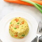 Yellow fried rice on a white plate with vegetables behind.