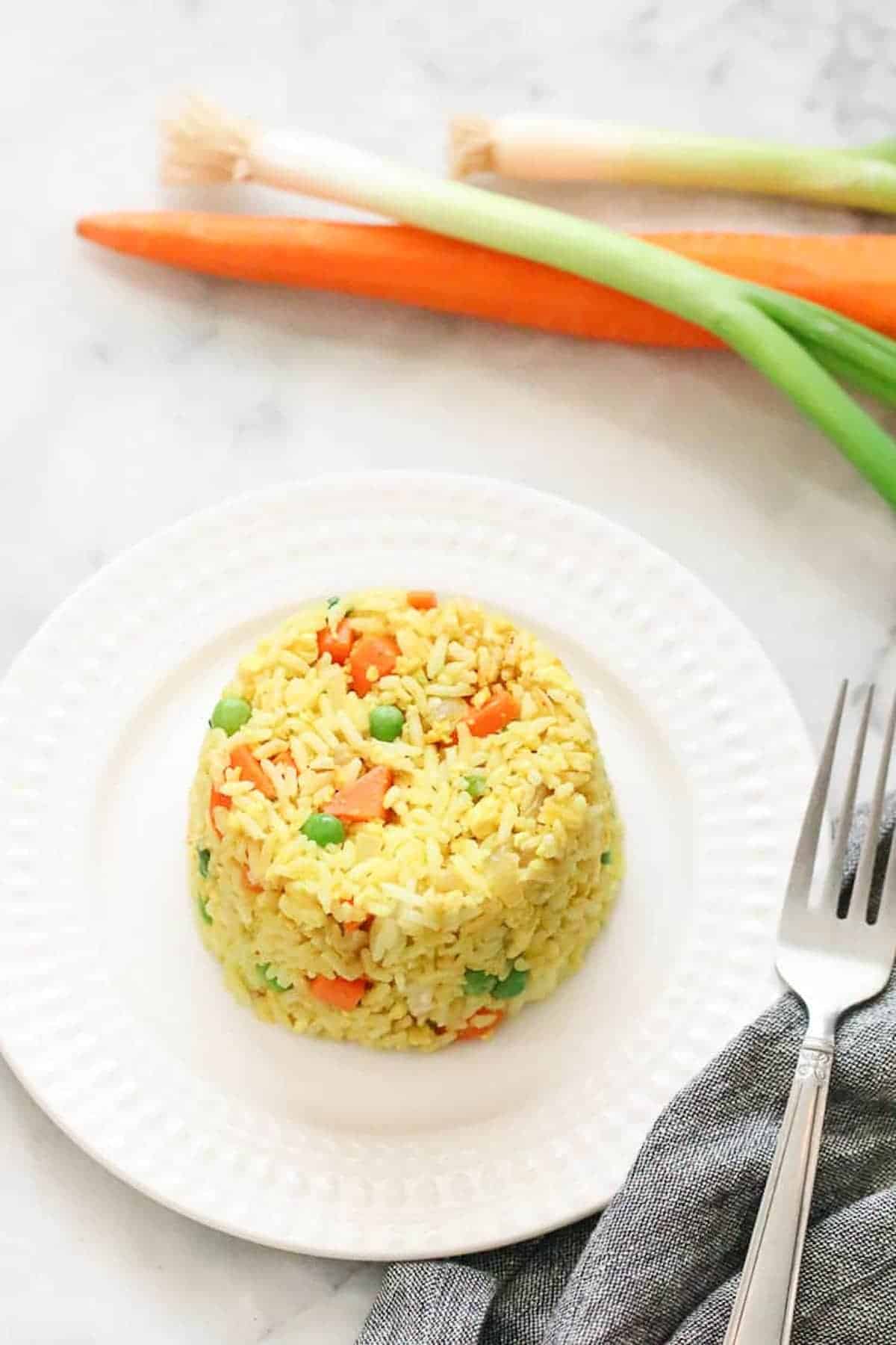 Yellow fried rice on a white plate with vegetables behind.