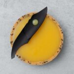 Close-up of a vibrant yellow yuzu tart with a black sesame crust.