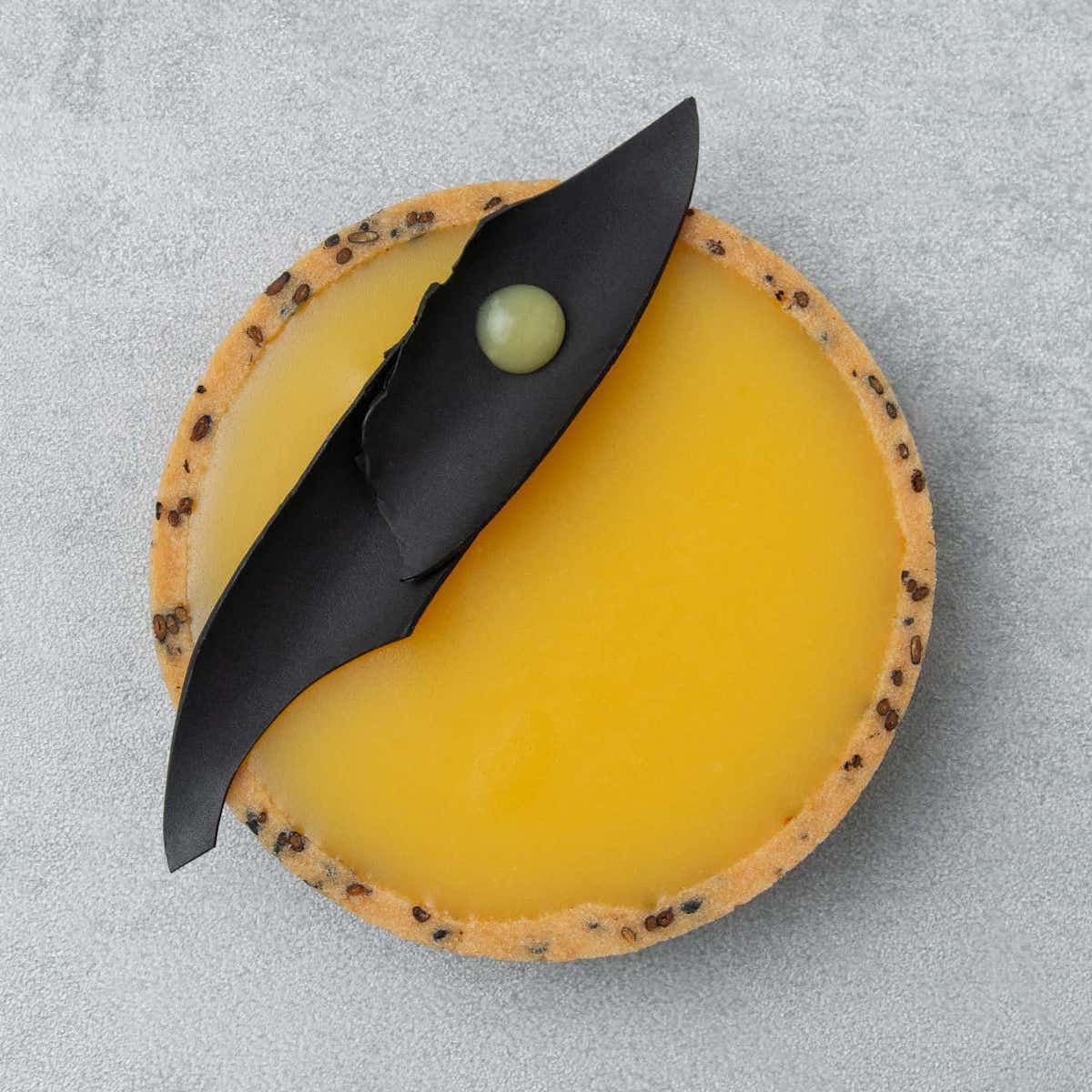 Close-up of a vibrant yellow yuzu tart with a black sesame crust.