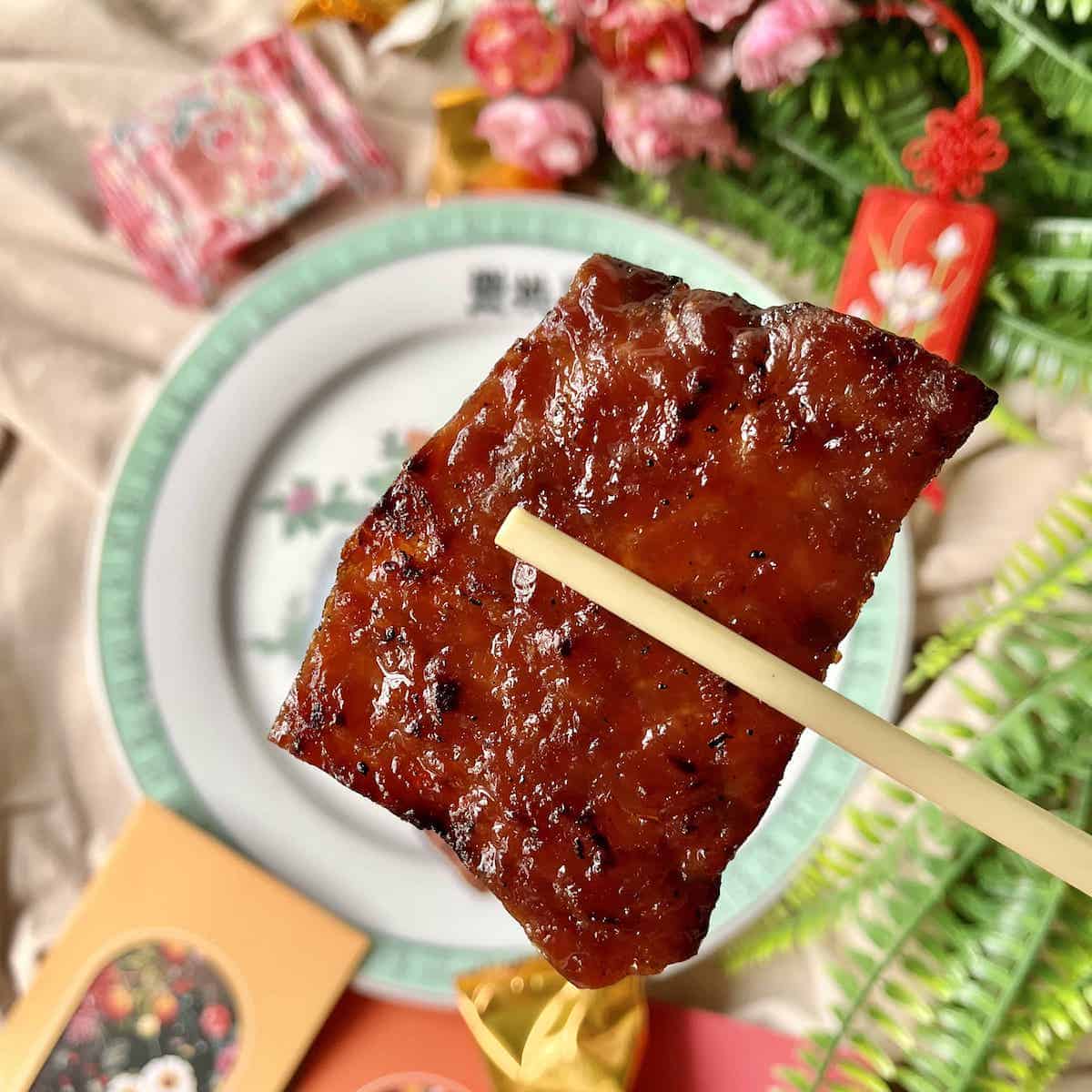 A piece of Chinese pork jerky held up by a pair of chopsticks.