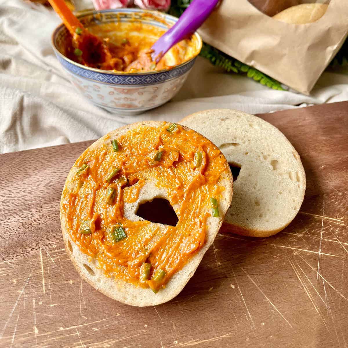 Half of a bagel covered with creamy gochujang butter sauce.